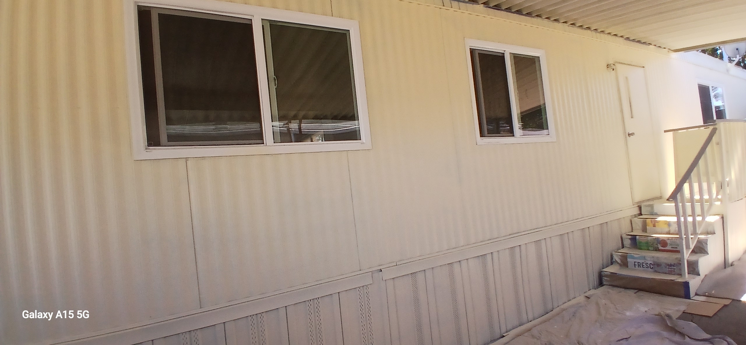 Side of the home with windows and steps to the entrance beneath the carport roof