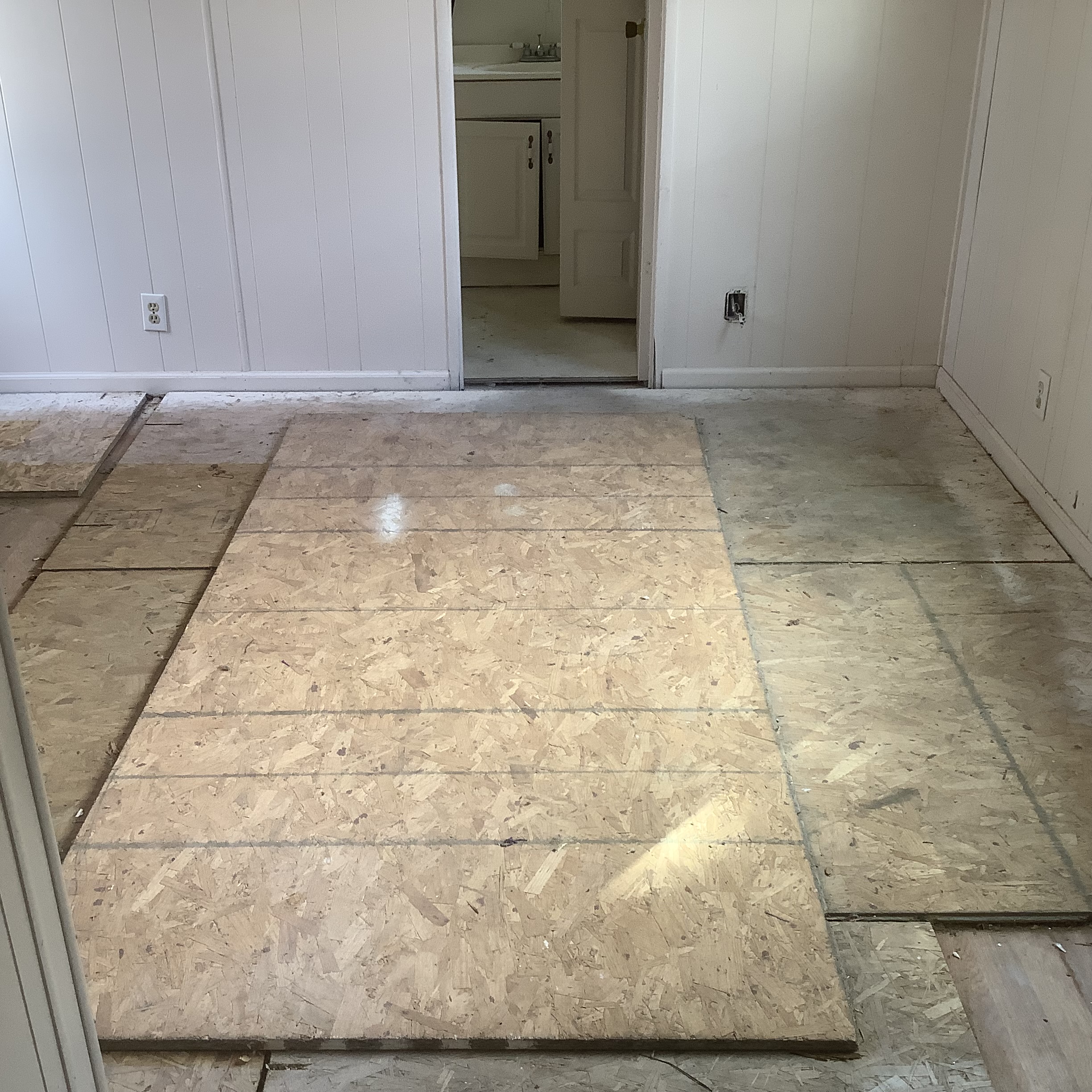 Interior room with exposed subfloor and a doorway to a bathroom