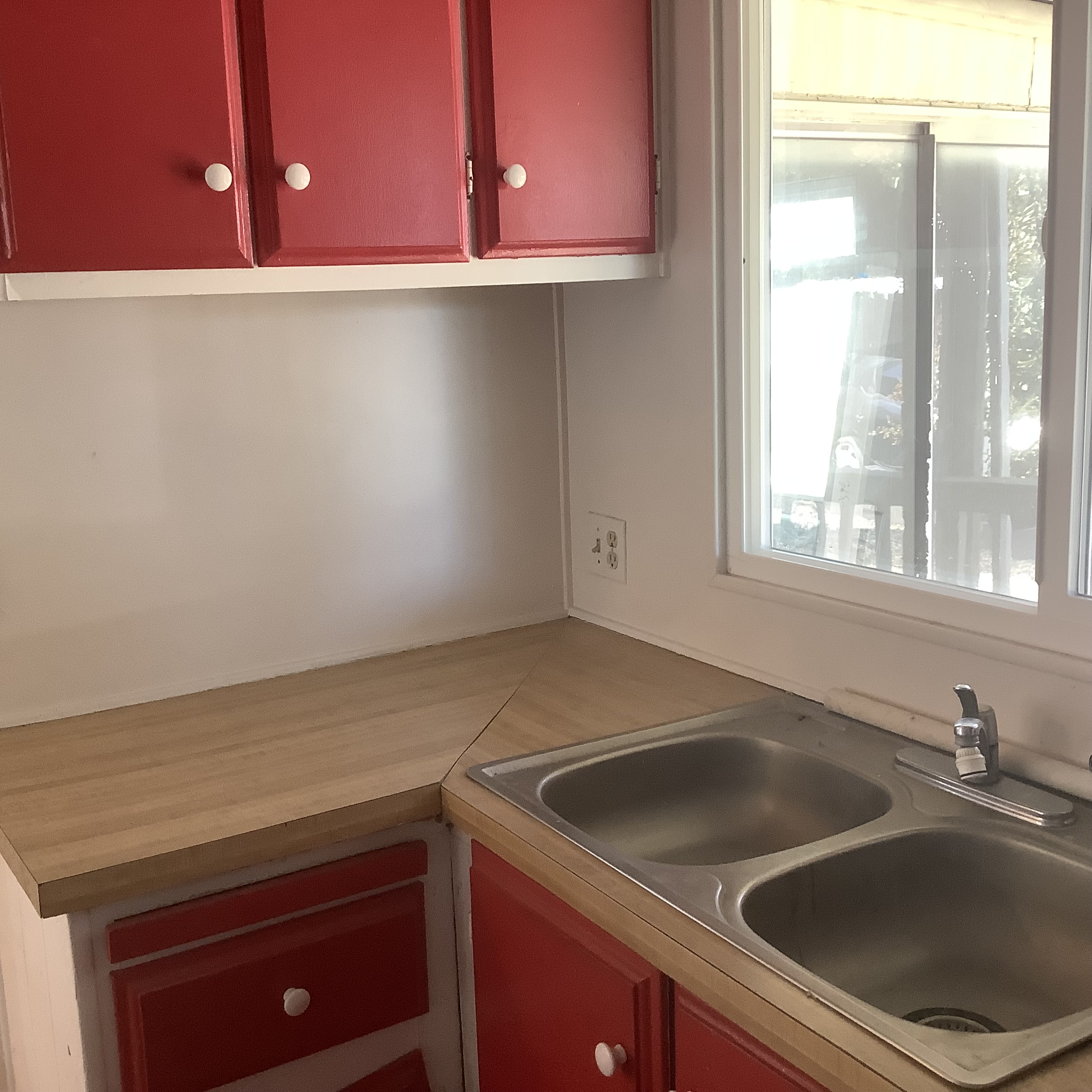 Double kitchen sink and countertop beneath red cabinets and a window